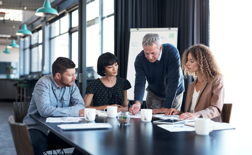 Businessman standing over group of colleagues and writing on notepad during meeting.