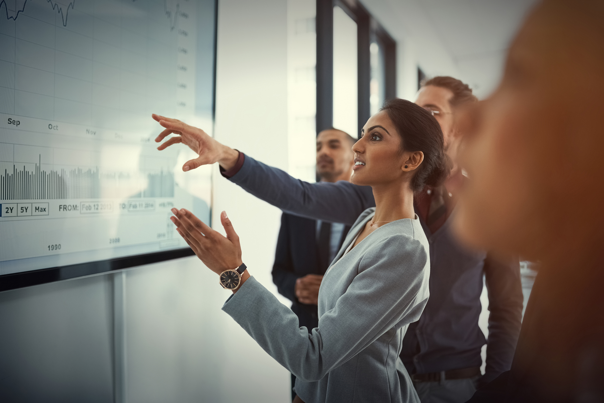 Businesswoman showing her colleagues a data model on a large screen in a boardroom.