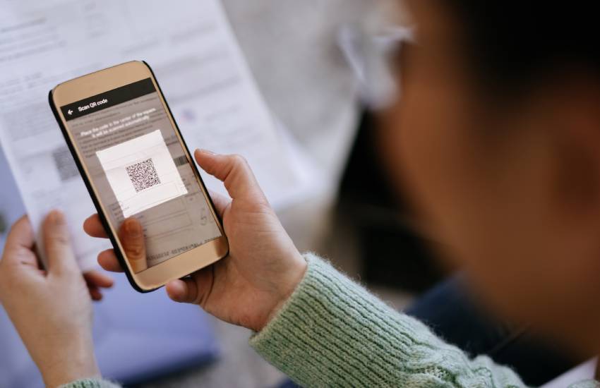 Elderly female patient holds her phone and uses the QR camera to scan a document's QR code.