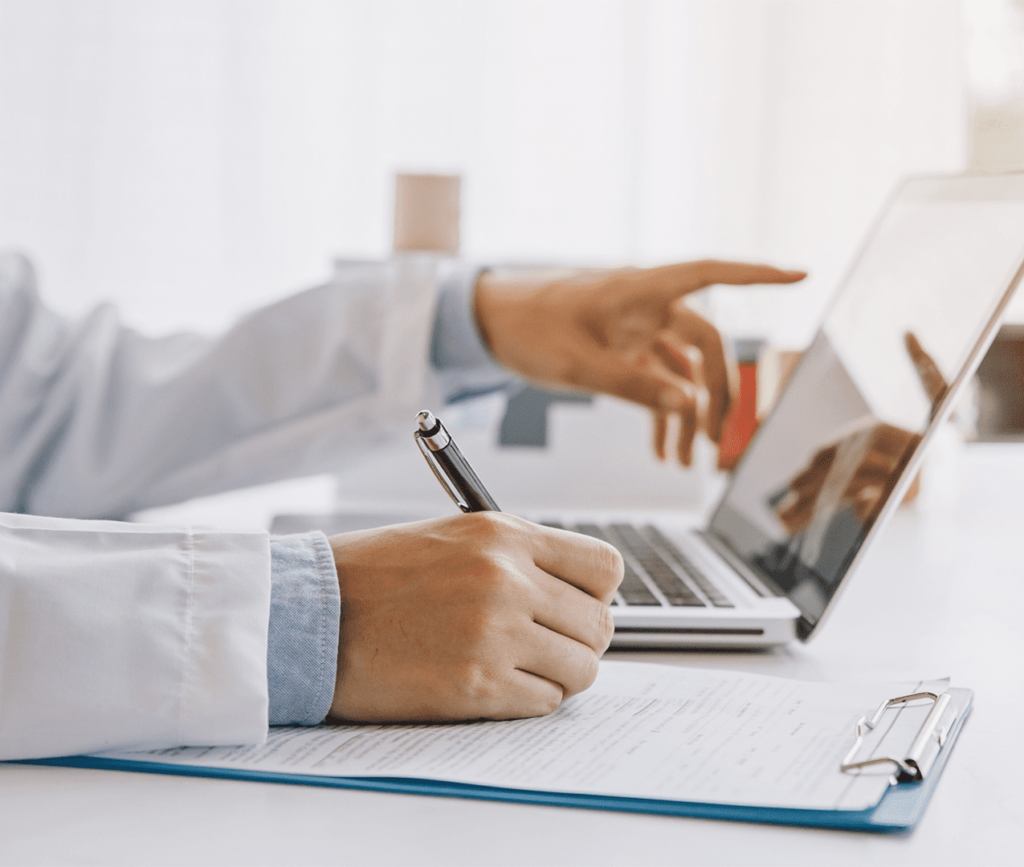 Close up photo of male doctor reviewing his computer and making notes on a clipboard
