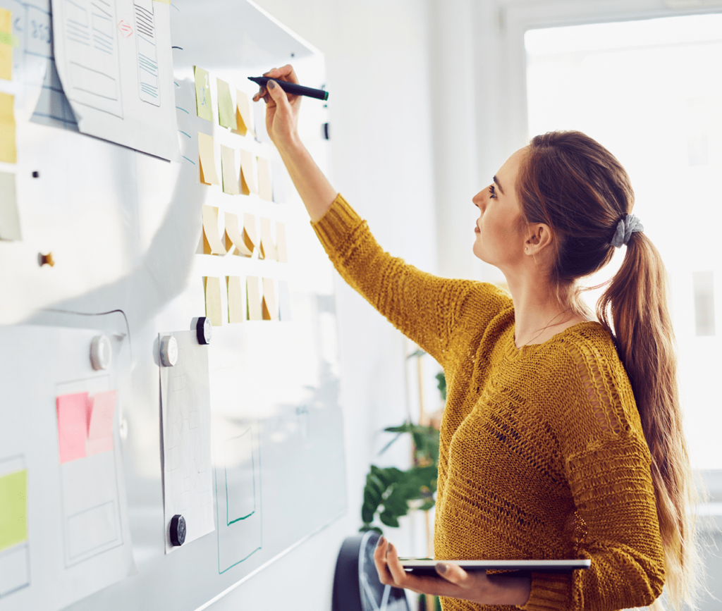 Business woman outlines a decision tree and wireframe on a whiteboard holding her tablet