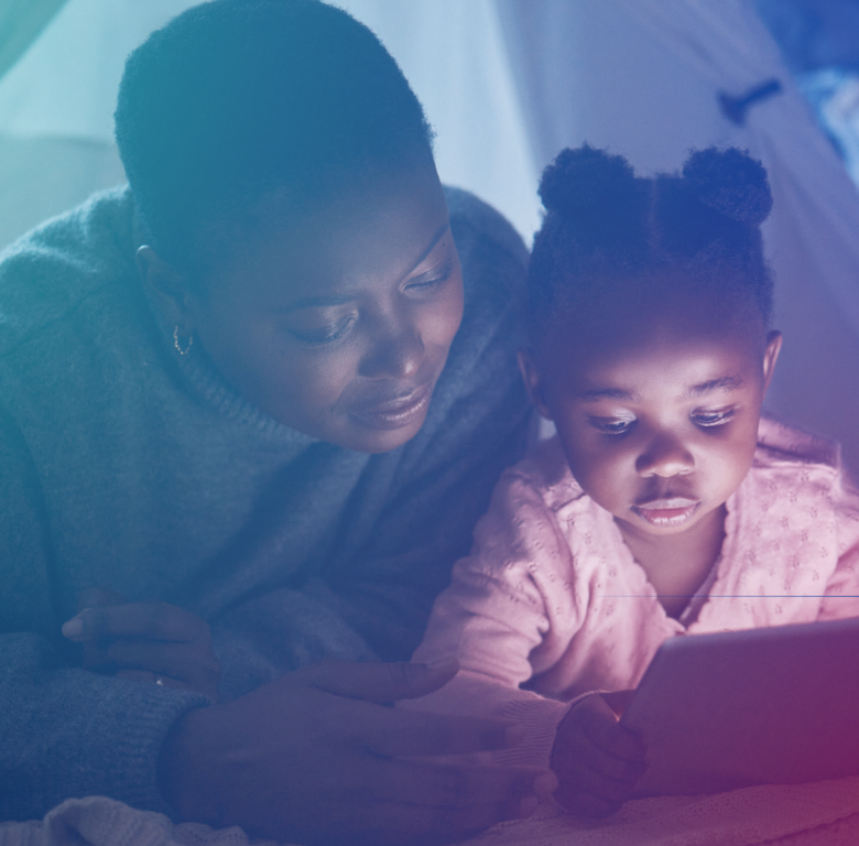 A mother and child lie down, looking at a glowing tablet screen in the dark.