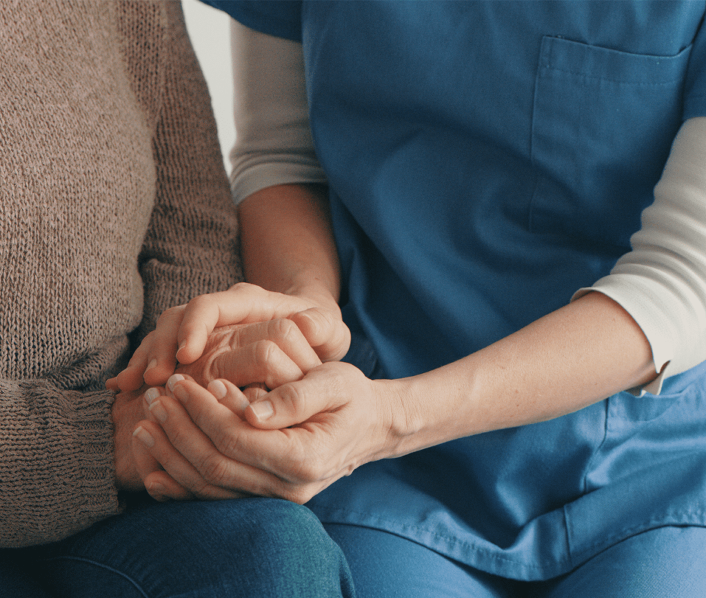 Close up of nurse and patient holding hands as the nurse comforts the older patient.