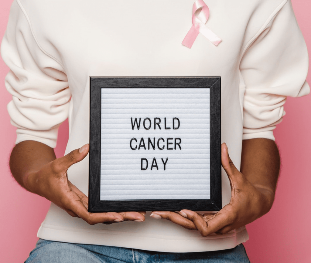 Person holding sign that says "World Cancer Day" and has a pink cancer support ribbon pinned to their shirt.