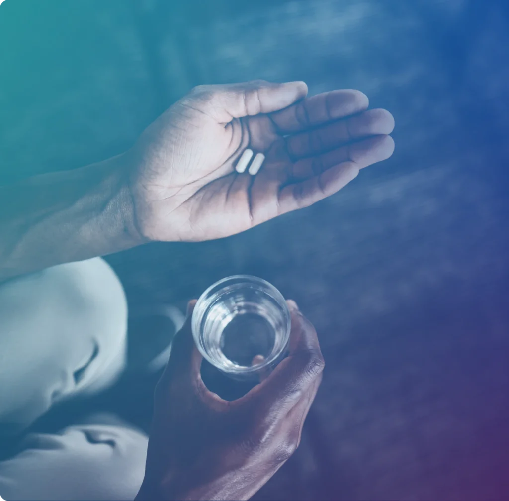 Hands holding two white pills in one palm and a clear glass of water in the other.