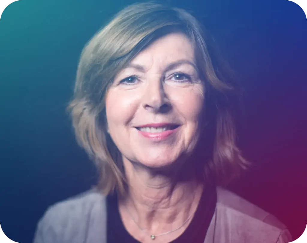 A smiling older woman with short brown hair and a light-colored top, against a dark background with a colorful gradient.
